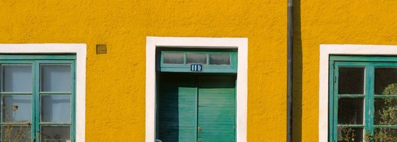 Yellow house with green windows and door.
